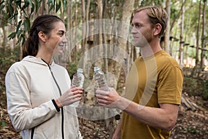Couple looking at each other holding water bottle in there hands in the forest