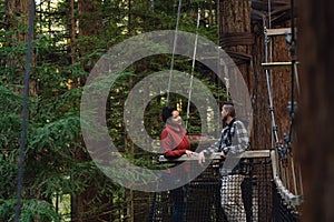 Couple looking each other on platform of a hanging bridge on red wood forest