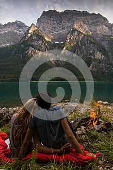 Couple looking at each other and relaxing in the front of a beautiful lake from Switzerland with fire beside.