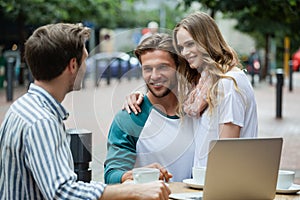 Couple looking at friend while sitting at sidewalk cafe