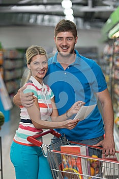 Couple Looking At The Grocery List In Supermarket