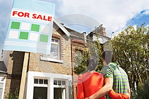 Couple Looking At New Home With For Sale Sign