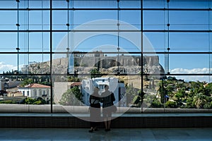 Couple looking out at the Acropolis throught huge glass window in the Acropolis Museum. Athens, Greece.