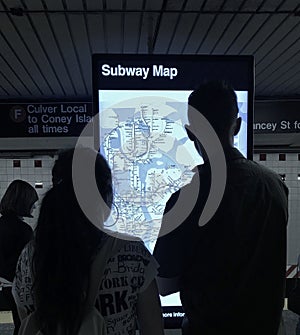 Couple Looking at Subway Information Digital Screen for Directions on NYC Subway Map MTA Train Station