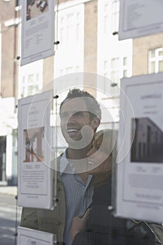 Couple Looking Through Window At Estate Agents