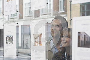 Couple Looking Through Window At Estate Agents