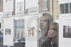 Couple Looking Through Window At Estate Agents