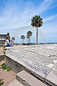 A couple looks sits on an embankment at Castillo De San Marcos while gazing on to Mantazas River