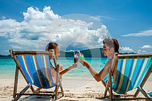 Couple in loungers clinking their glasses on a tropical beach