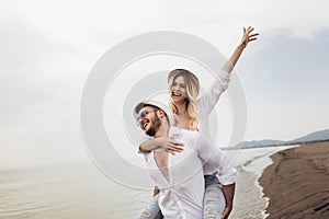 Couple in love on beach summer vacations. Joyful girl piggybacking on young boyfriend having fun