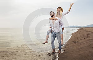 Couple in love on beach summer vacations. Joyful girl piggybacking on young boyfriend having fun