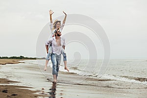 Couple in love on beach summer vacations. Joyful girl piggybacking on young boyfriend having fun