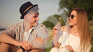 Couple in love blowing blowballs flowers in faces of each other. Smiling and laughing people having good time outside on summer