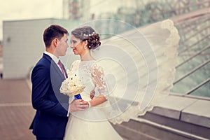 Couple in love bride and groom embrace on a background of urban architecture. The bride's veil fluttering in the wind