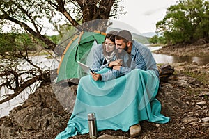 Couple in love camping forest hike.  Couple sitting near tent using digital tablet