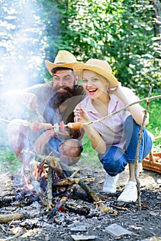 Couple in love camping forest roasting sausage at bonfire. Traditional roasted food as attribute of picnic. Camping and