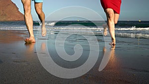 Couple in love carefree running from the water and waving their hands to someone on the beach. Picturesque ocean coast