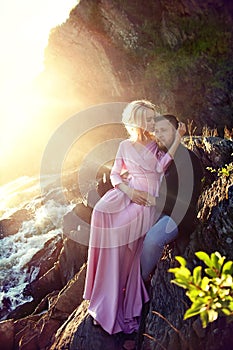 Couple in love close-up sitting on a stone on a beautiful Sunny day at sunset. Love emotions and hugs in the sun. Blonde woman