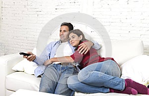 Couple in love cuddling on home couch relaxing watching movie on television with man holding remote control