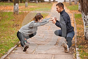 A couple are doing sports in the park in the fall. Stretch muscles holding hands.