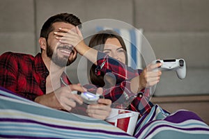 Couple in love enjoying their free time, sitting on a couch next to the window, playing video games and having fun.