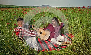 couple in love with guitar and camera. man and woman photographing in poppy flower field. summer vacation. happy family