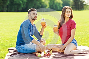 Couple in love have fun in the park and drink smoothies and eating fruit at a picnic