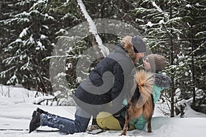 Couple in love having fun with dog in the snow in forest