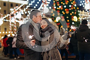Couple in love having fun with sparklers on christmas decoration lights street. Romantic date for Valentine`s day Outdoors. Young