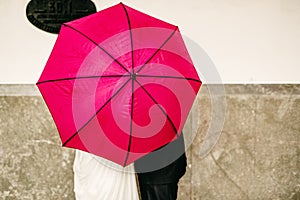 Couple in love hiding behind a big red umbrella while they kiss shyly hiding to keep their privacy and intimacy