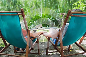 A couple in love hold hands sitting on two wooden beach chairs in the garden. Relaxing place concept