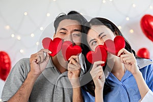 Couple in love holding red heart-shaped cards and smiling happy in Valentine's Day concept