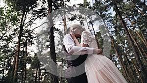 A couple in love is hugging in a beautiful pine forest. The girl in the white dress leaned against her boyfriend and put her hands