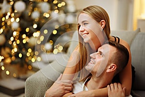 Couple in love kisses and hugs on the sofa near the Christmas tree lights. New year`s night. Christmas.