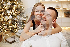 Couple in love kisses and hugs on the sofa near the Christmas tree lights. New year`s night. Christmas