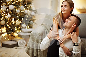 Couple in love kisses and hugs on the sofa near the Christmas tree lights. New year`s night. Christmas