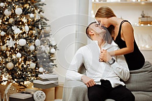 Couple in love kisses and hugs on the sofa near the Christmas tree lights. New year`s night. Christmas