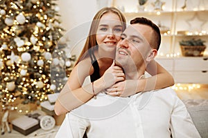 Couple in love kisses and hugs on the sofa near the Christmas tree lights. New year`s night. Christmas