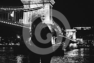 Couple in love is kissing and hugging near Chain bridge in Budapest. Night city lights in old european city. Man and woman