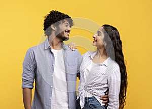 Couple in love. Loving couple embracing, looking and smiling to each other, standing over yellow studio background