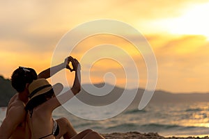 Couple in love making a heart - shape with hands on tropical on the sunset beach in holiday.