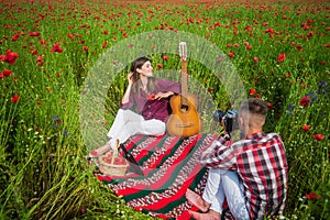 couple in love making photo on camera with acoustic guitar in summer poppy flower field, free time.