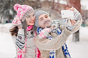 Couple in love making selfie on winter outdoors in sweaters, scarf and mittens