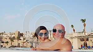 Couple in love, man and woman, in funny, identical, round sunglasses, hug and kiss, having fun, relaxing in water of