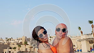 Couple in love, man and woman, in funny, identical, round sunglasses, hug and kiss, having fun, relaxing in water of