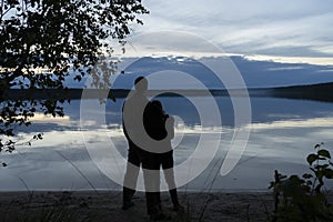 A couple in love - a man and a woman standing on the shore, in a romantic setting, admire the reflection of the evening clouds in