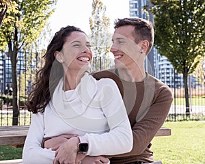 A couple in love millenials hugging each other on a bench and laughing with joy, outdoor couple life, love concept