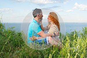 A couple in love outdoor. Lovers sitting hugged on the grass at lake bank in grass on water and sky background