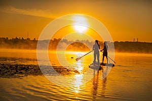 couple in love on paddle boards, sunrise, sky and fog over the water, romantic atmosphere