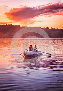 Couple in love ride in a rowing boat on the lake during sunset. Romantic sunset in golden hour. Happy woman and man together relax